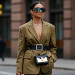 2025 Accessory Forecast: Elevate Your Style on a Budget Woman showcasing 2025 accessory trends with oversized belt, layered necklaces, mini-bag, and futuristic sunglasses.