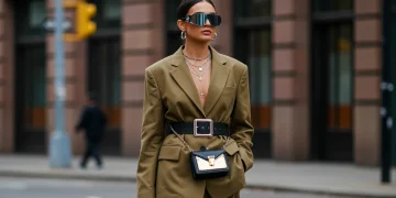 Woman showcasing 2025 accessory trends with oversized belt, layered necklaces, mini-bag, and futuristic sunglasses.